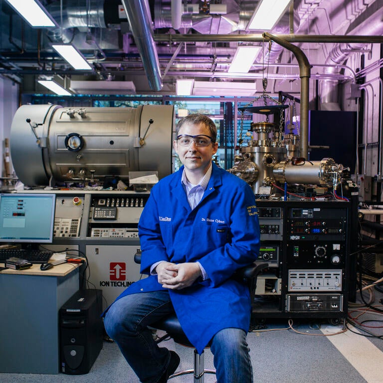 researcher sitting on a stool wearing ppe in front of equipment